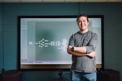 Josh Taibbi stands in front of a screen displaying programming for the interactive light wall exhibit he developed.