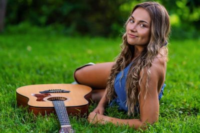 Annalyse Hasty lounges in the grass next to an accousitc guitar.