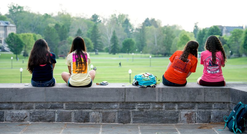 Students sitting at the pylons, staring out at the drillfield. One leans over to speak to student next to them. 